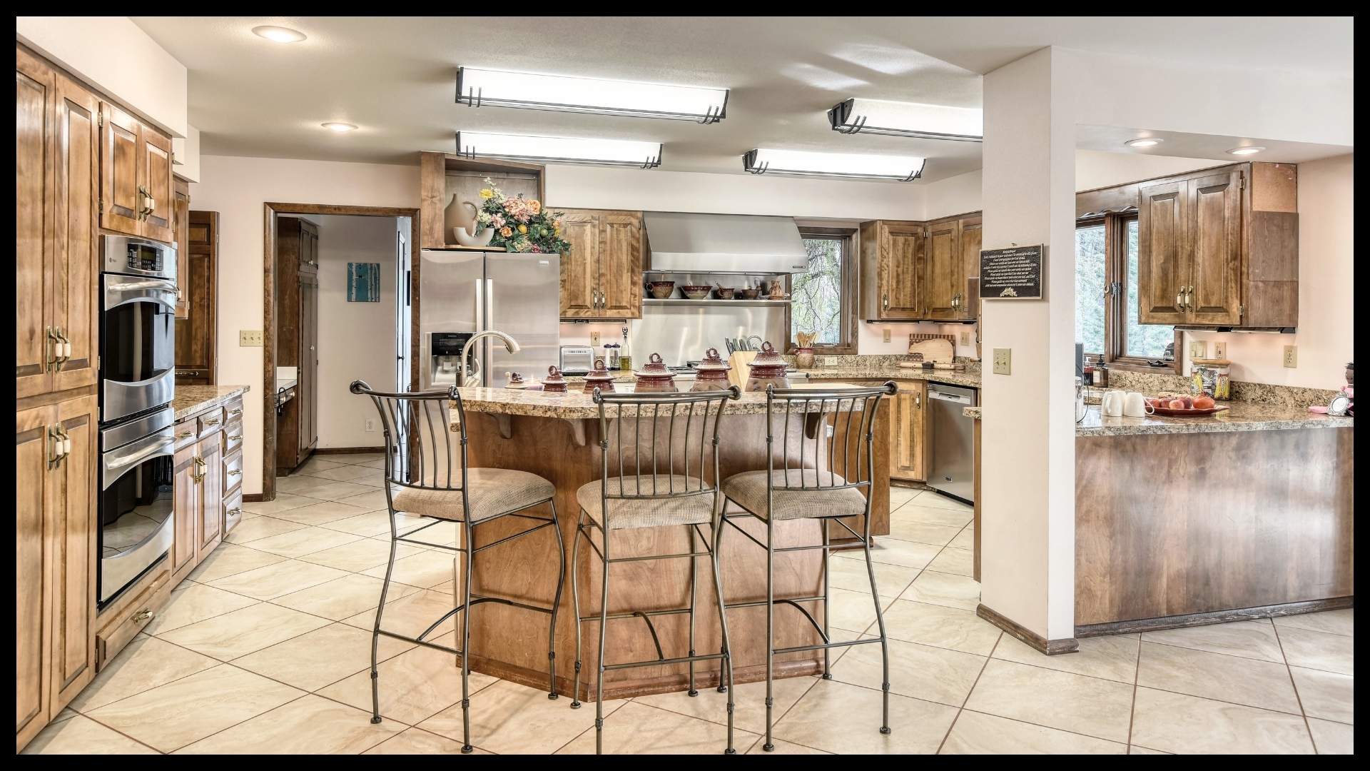 spacious chef’s kitchen with granite countertops, wood cabinetry, stainless steel appliances, and breakfast bar in a North Idaho ranch home