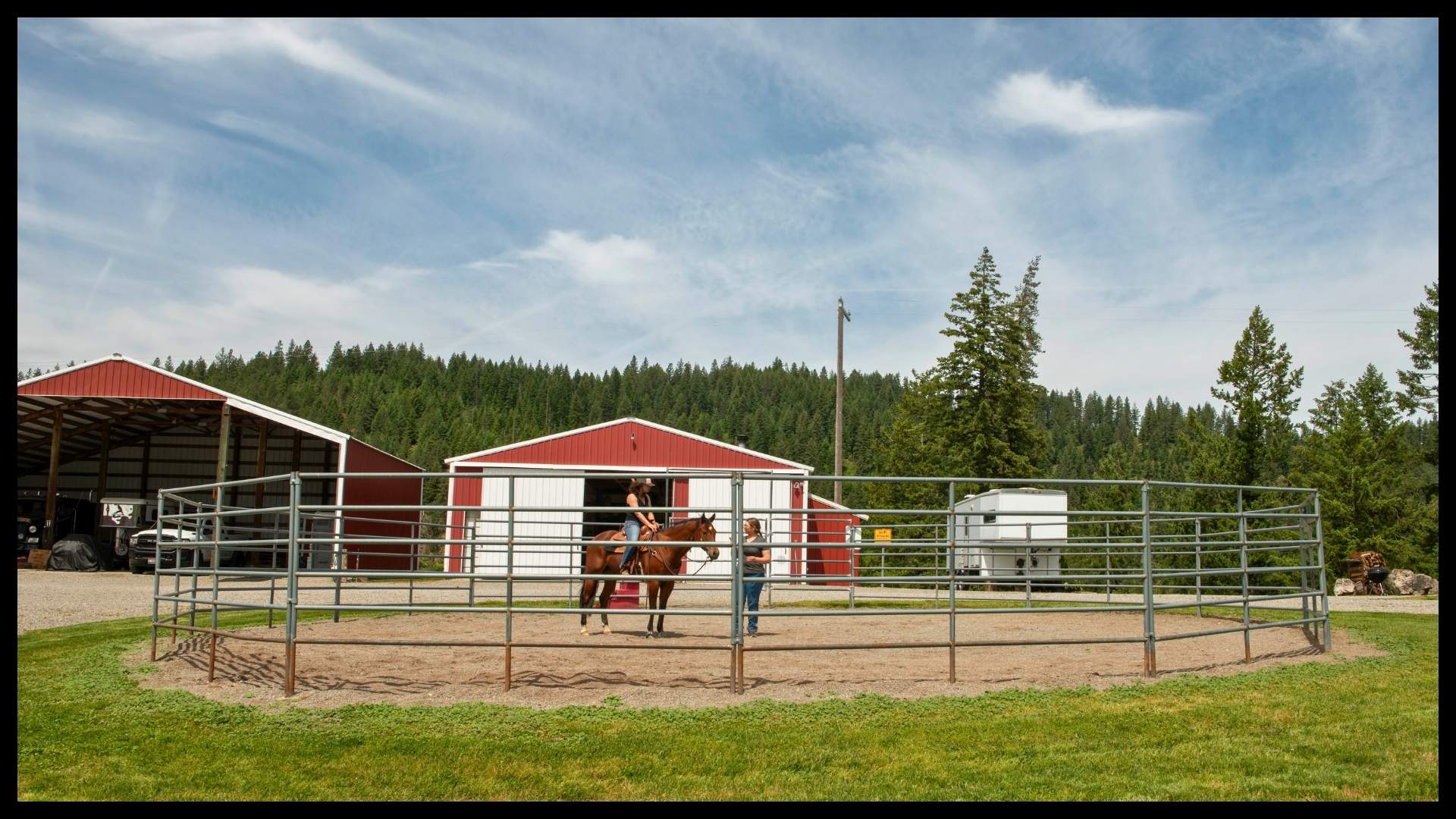 red barn and covered arena with round pen for horse training at North Idaho ranch surrounded by forested hills